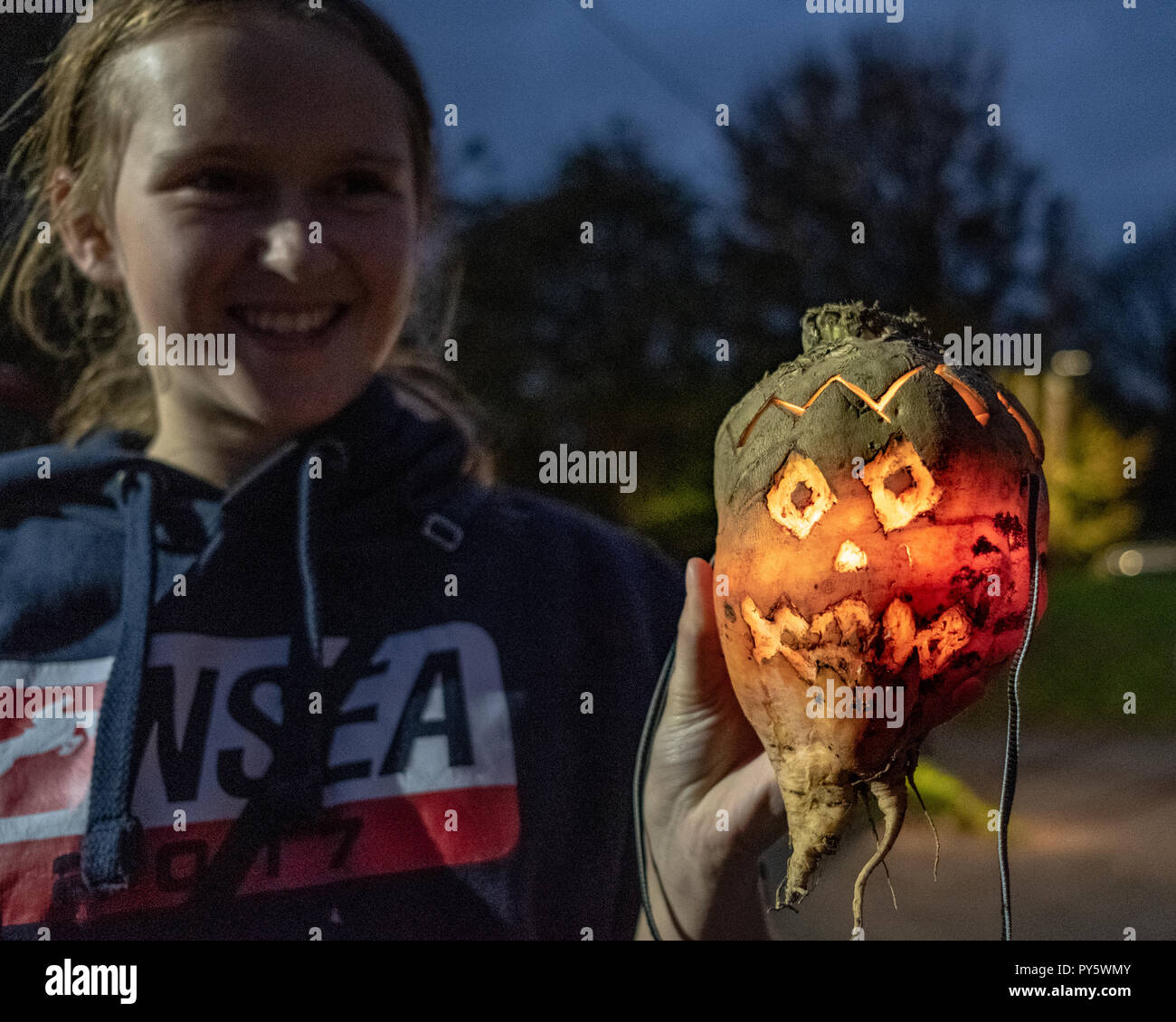 Hinton St George, Somerset, UK - 25 October 2018.  A young woman holds a 'Punkie' during the annual 'punkie night' procession around Hinton St George village. A 'Punkie' is a hollowed out mangold or mangle-wrurzel with a lit candle inside to make a lantern. Although the origins of the custom are obscure legend has it that the wives of Hinton St George went to met their husbands as they came back from the Chiselbrough Fair, held on the last Thursday in October. They made lanterns out of hollowed out mangle-wurzels to light their way. Credit: Tom Corban/Alamy Live News Stock Photo