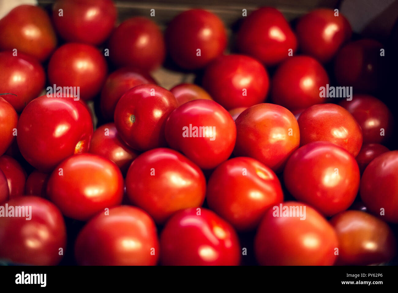 A group of small, shiny red tomates for sale at a market Stock Photo