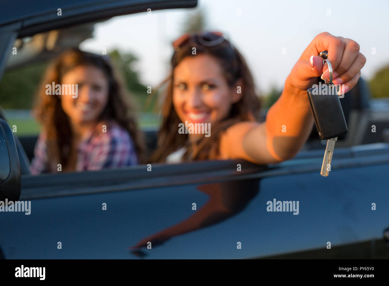 Beautiful young woman reaching out car keys to the camera while smiling at the camera Stock Photo