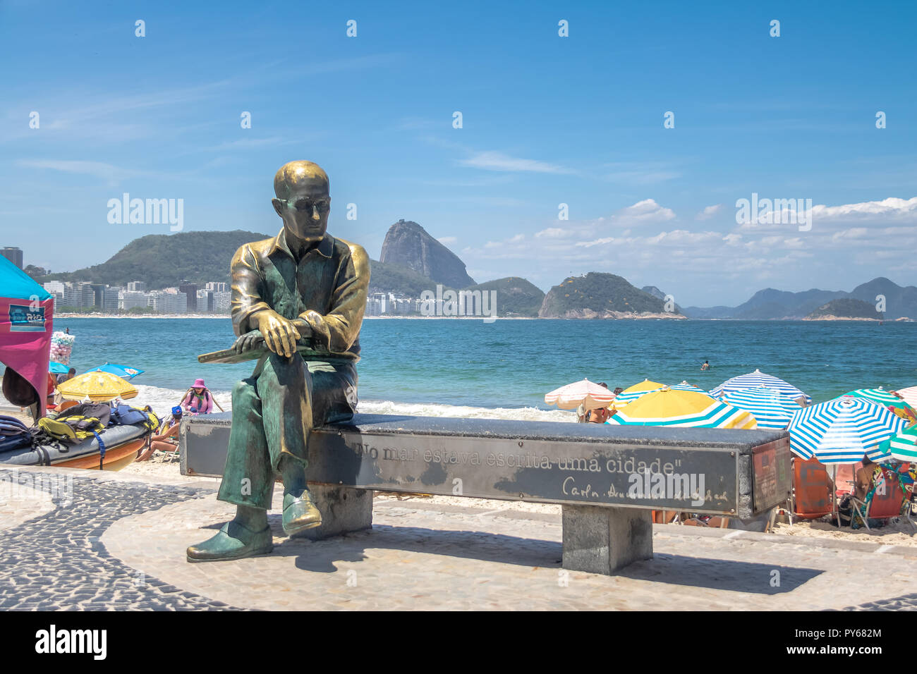 Carlos Drummond de Andrade Statue at Copacabana Beach with Sugar Loaf Mountain on background - Rio de Janeiro, Brazil Stock Photo
