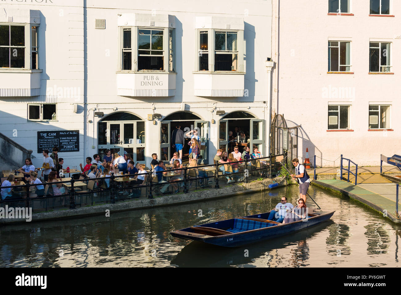 People sat outside the Anchor pub by the river Cam as a punt boat goes by, Cambridge, UK Stock Photo