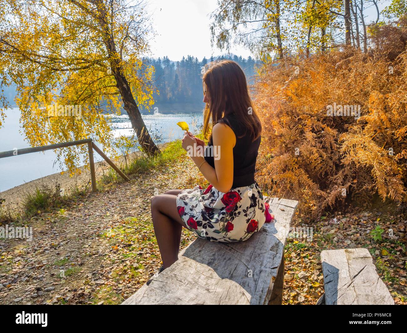 Sitting near lake in countryside young woman is sitting holding one single Autumn leaf in hands nostalgia nostalgic Stock Photo