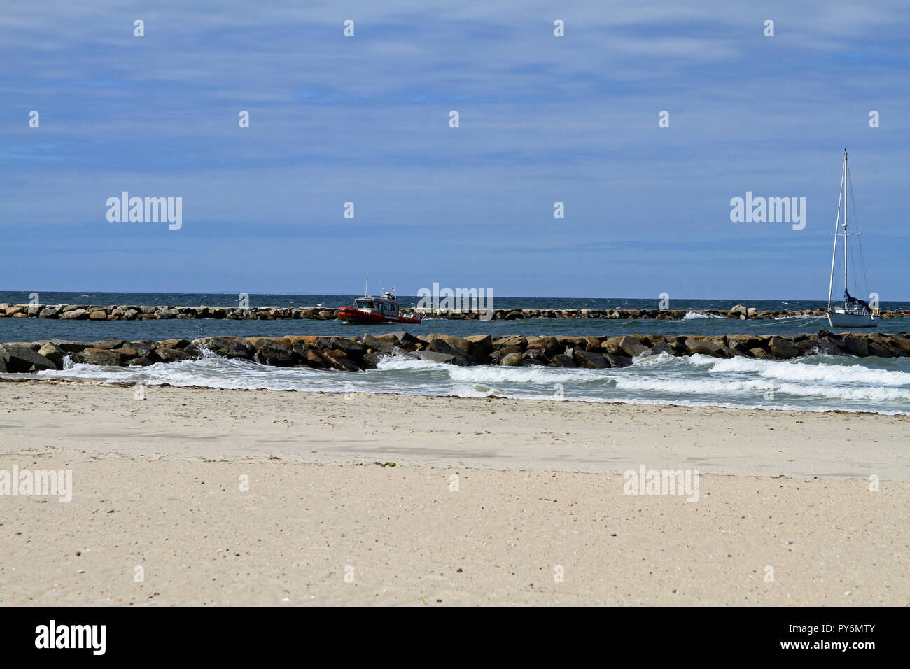 A disabled sailboat being pulled by a TowBoat U.S. through the jetty marking the entrance to Sesuit Harbor on Cape Cod in East Dennis, Massachusetts Stock Photo