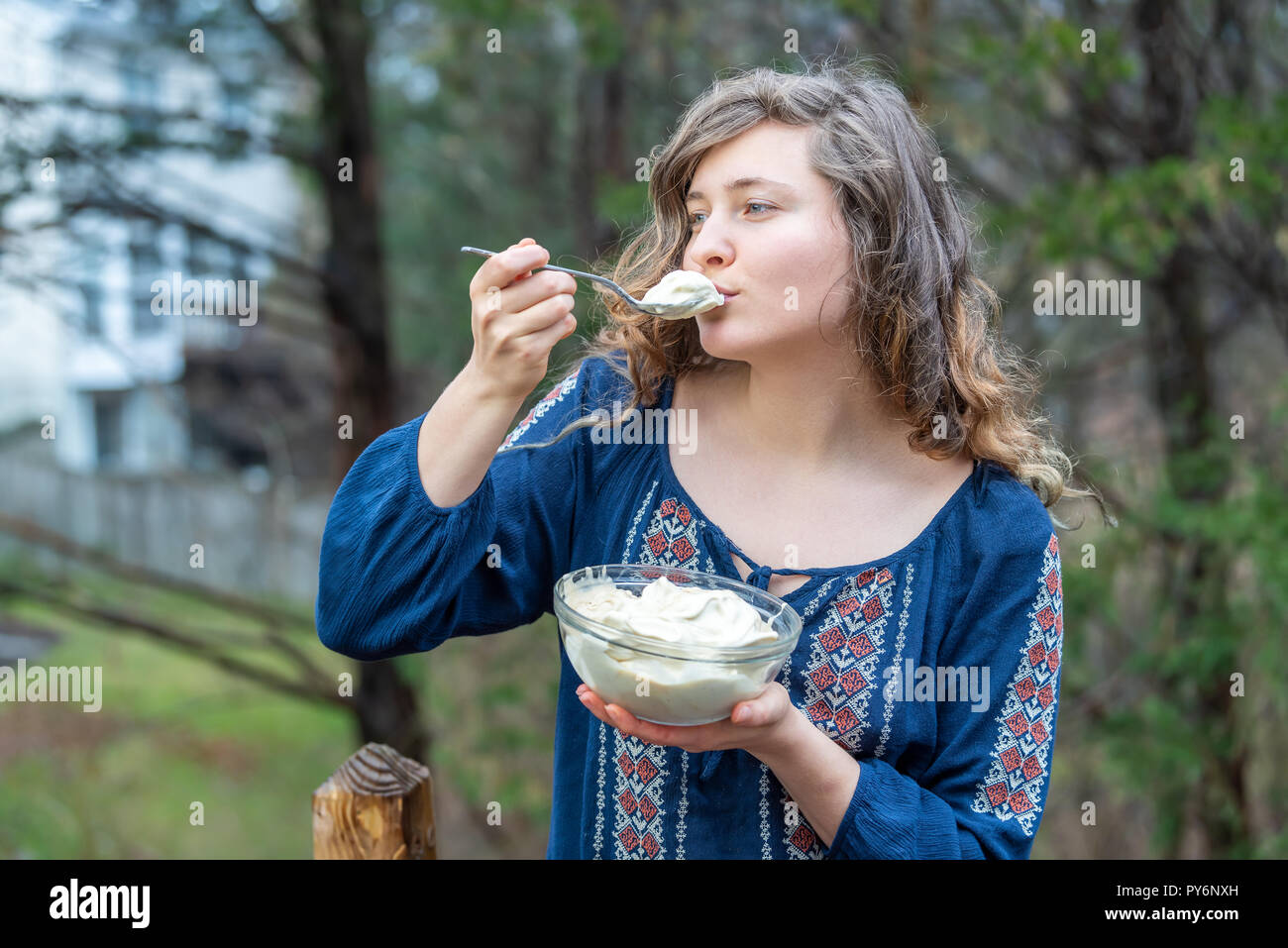 Young woman outside, outdoors, holding glass bowl full of homemade, raw vegan vanilla ice cream, scooping scoop with spoon in one hand, eating, tastin Stock Photo