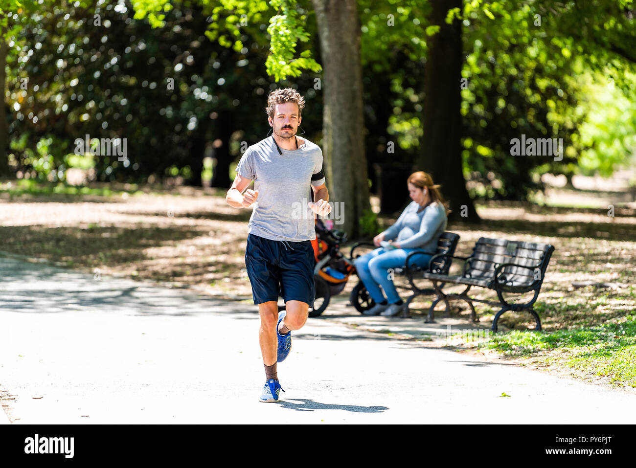 Atlanta, USA - April 20, 2018: Man running jogging on sunny bright day in shorts listening to music in Piedmont Park trail path road in Georgia city i Stock Photo