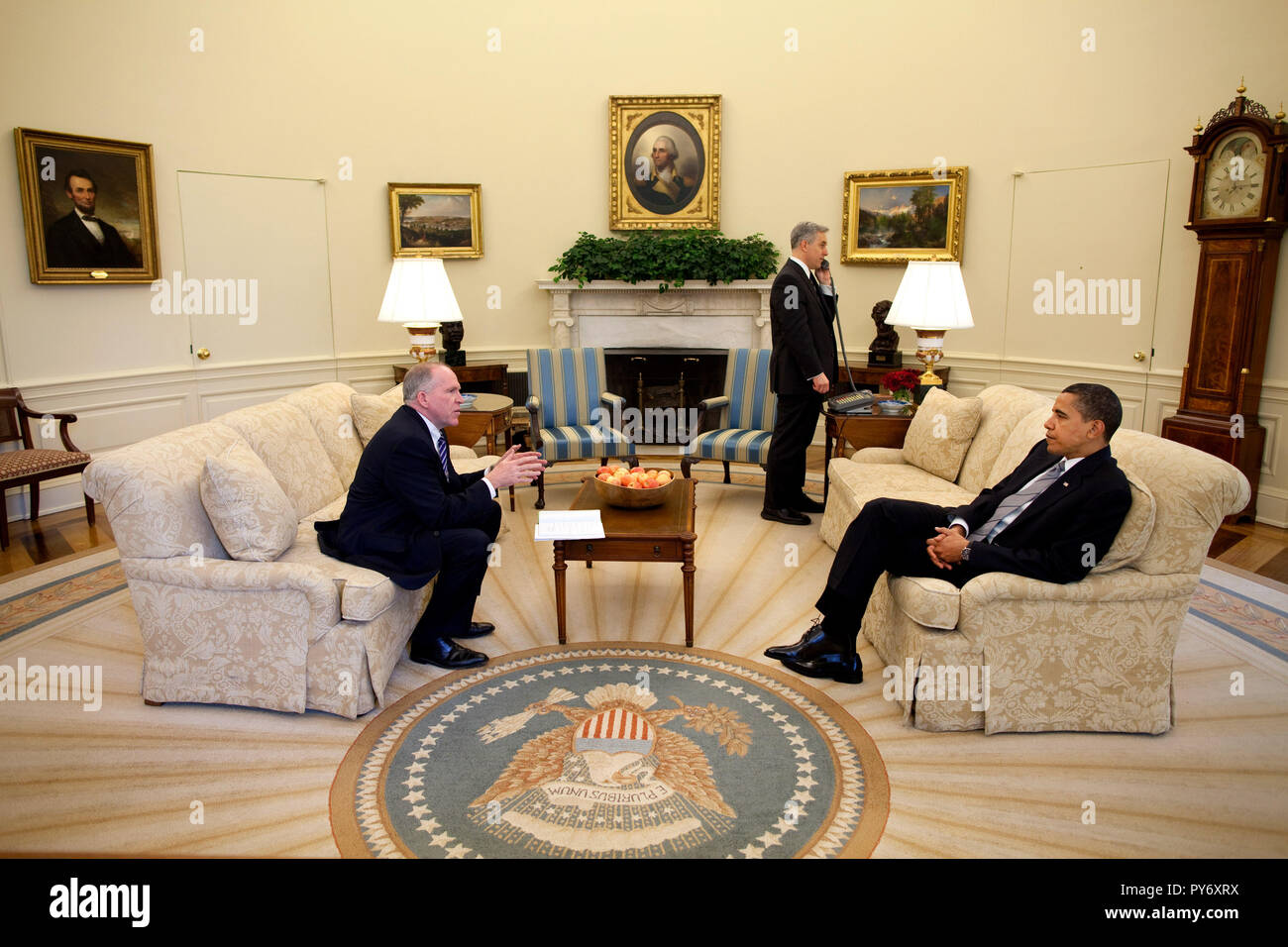 President Barack Obama talks with John Brennan, assistant to the President for Homeland Security,  while a National Security Council staff member places a call to a foreign leader in the Oval Offie May 7, 2009.  Official White House Photo by Pete Souza. This official White House photograph is being made available for publication by news organizations and/or for personal use printing by the subject(s) of the photograph. The photograph may not be manipulated in any way or used in materials, advertisements, products, or promotions that in any way suggest approval or endorsement of the President,  Stock Photo