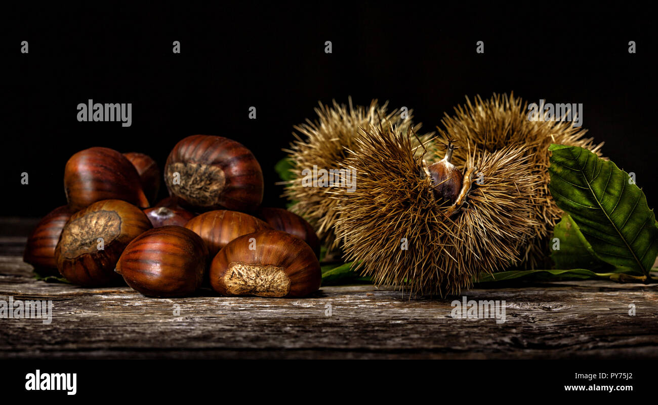 Chestnuts and chestnut bur on wooden table. Light painting technique. Stock Photo
