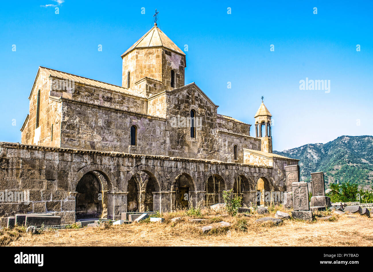 Odzun monastery on the south side  with views of the arched  gallery with the bell tower and stone crosses  in the background of forested mountains Stock Photo