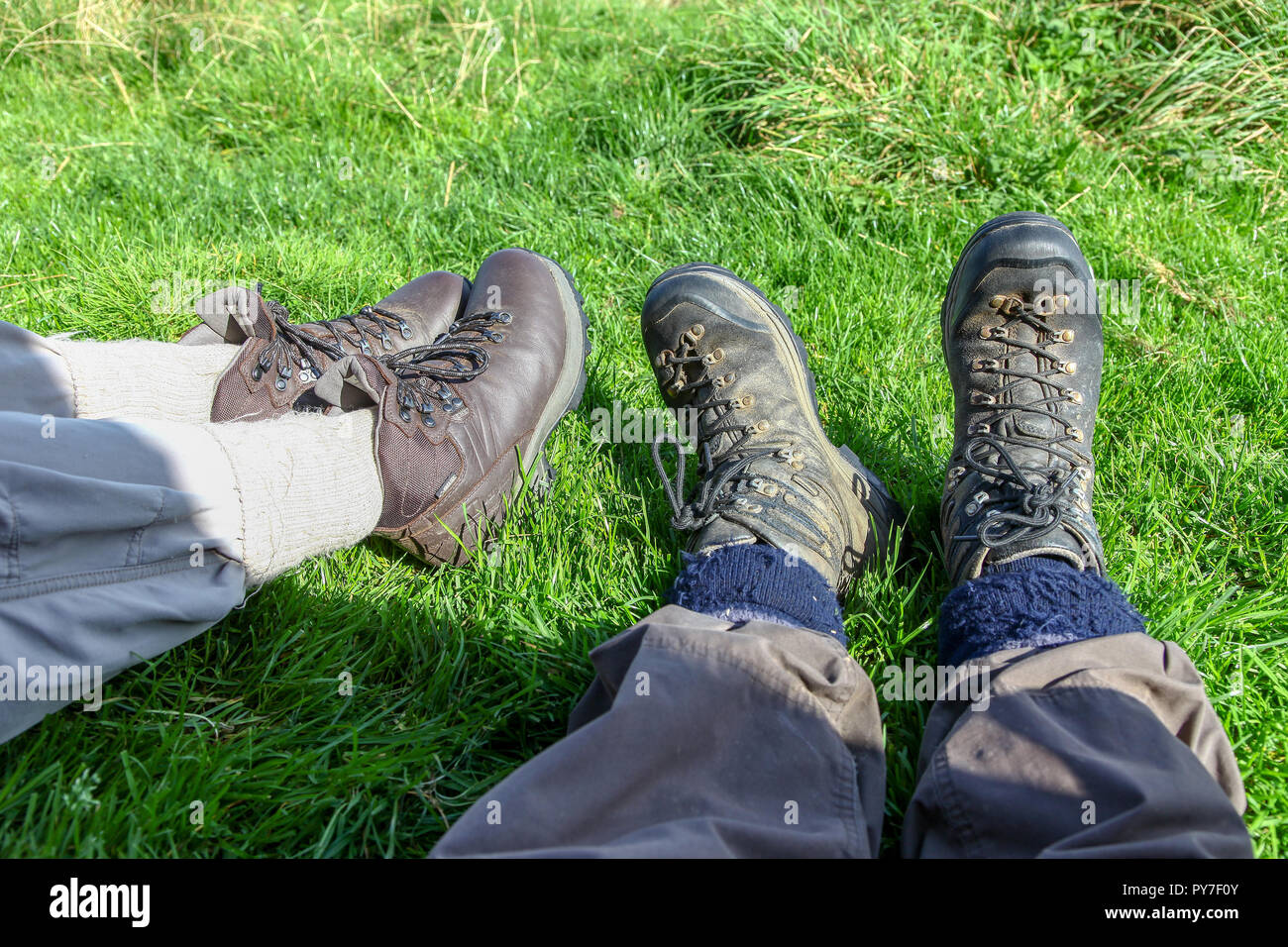 A man and a woman wearing walking boots lying down on the grass Stock Photo