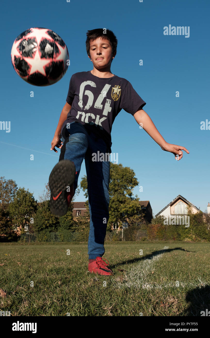 UK, 11 years old boy kicking a football ball in the park Stock Photo