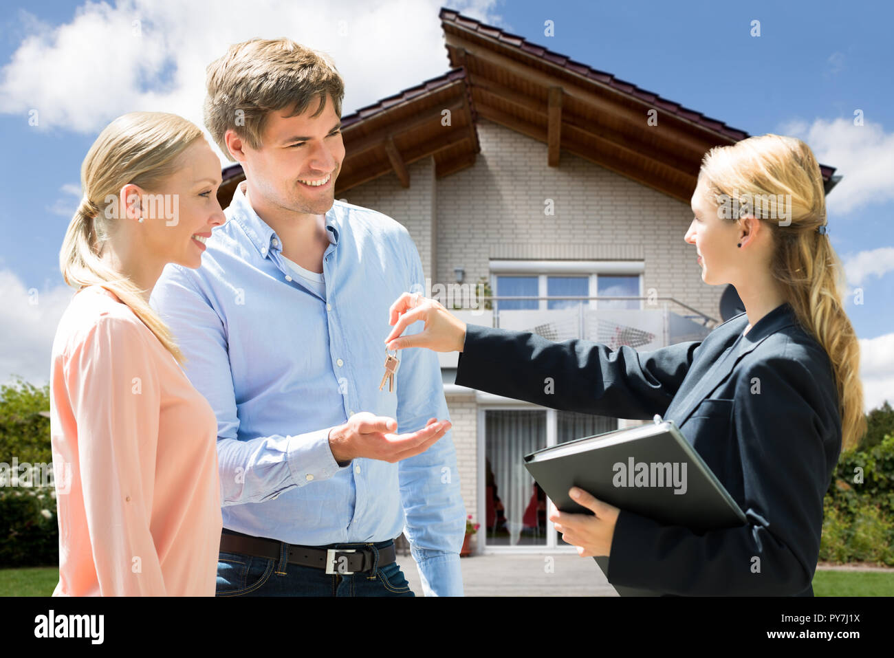 Smiling Female Real Estate Agent Giving Key Of New House To Young ...