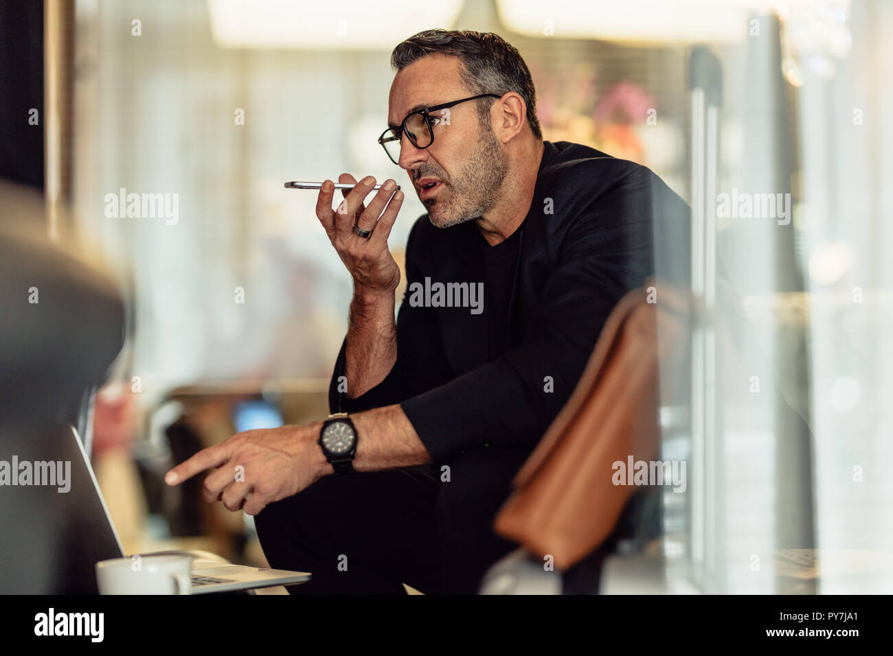 Mature businessman sitting in the hotel lobby with laptop making phone call. Male entrepreneur sitting in hotel waiting area making call. Stock Photo