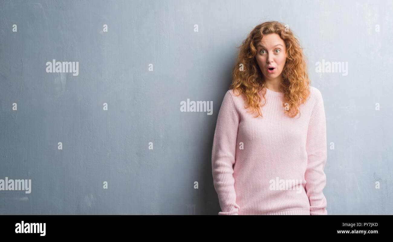 Pink Scared Young redhead woman over grey grunge wall wearing pink sweater afraid ...