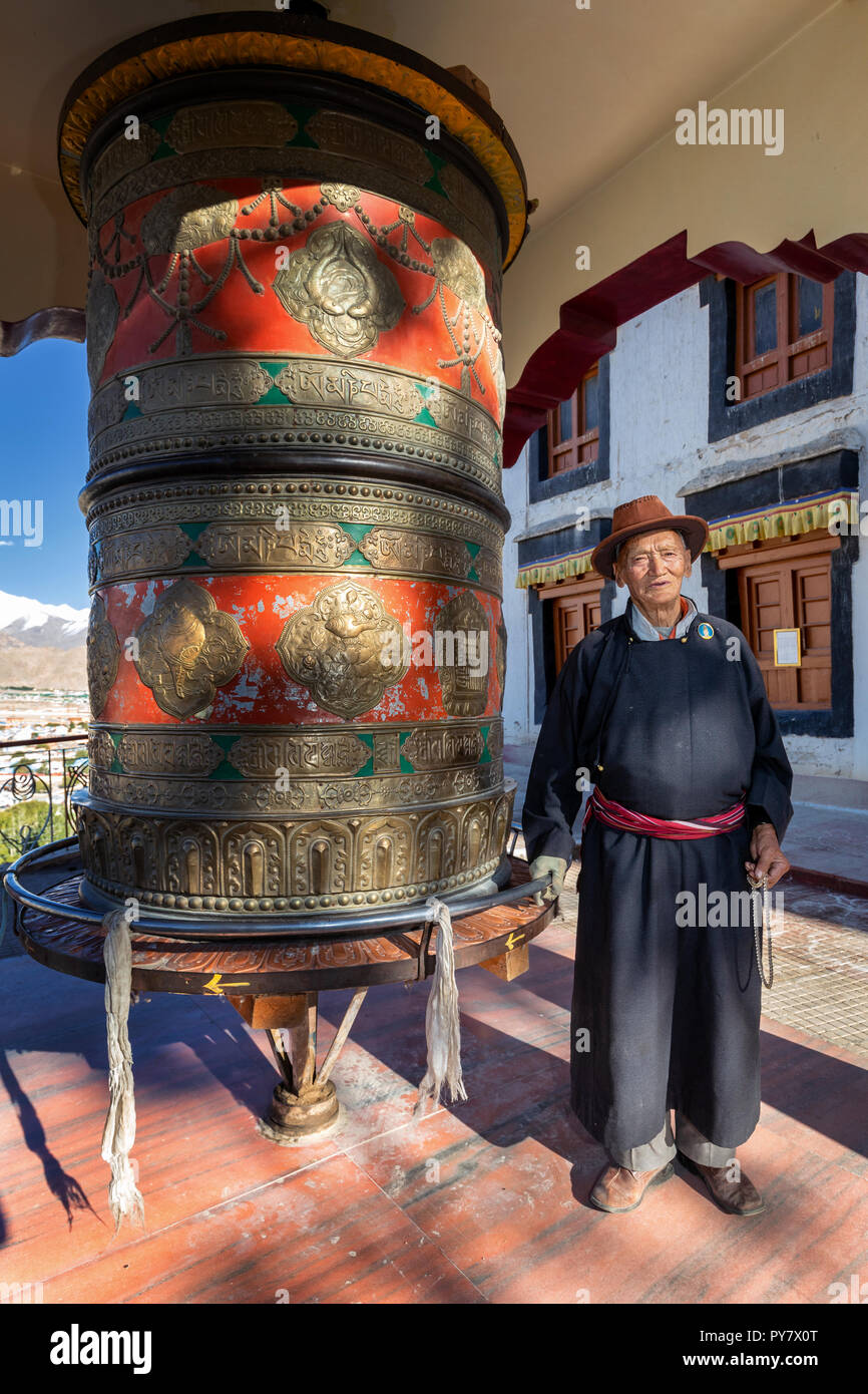Elderly man with a large prayer wheel in front of Spituk Gompa, Leh district, Ladakh, India Stock Photo