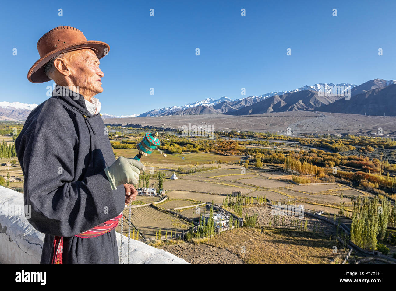 Elderly man with a prayer wheel watching the landscape around  Spituk Gompa, Leh district, Ladakh, Kashmir, India Stock Photo