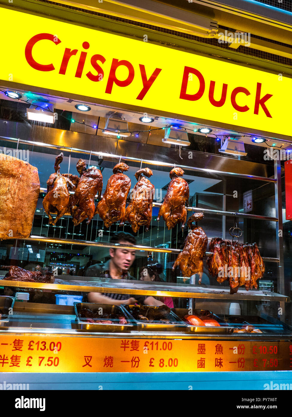 CRISPY DUCK WINDOW DISPLAY CHINATOWN Chef arranging duck & pork hanging air drying in Chinese restaurant Gerrard Street Chinatown Soho London UK Stock Photo