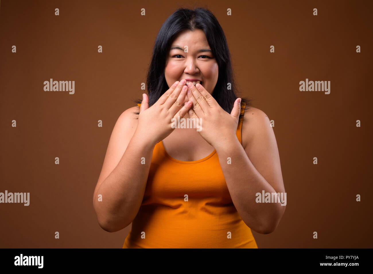 Happy overweight Asian woman laughing and covering mouth Stock Photo