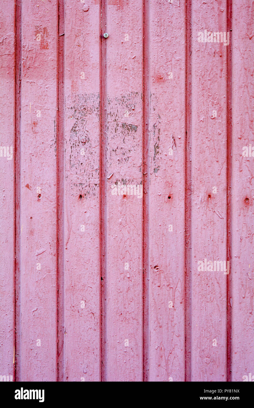 An old distressed wooden vertical plank texture with dry peeling pink
