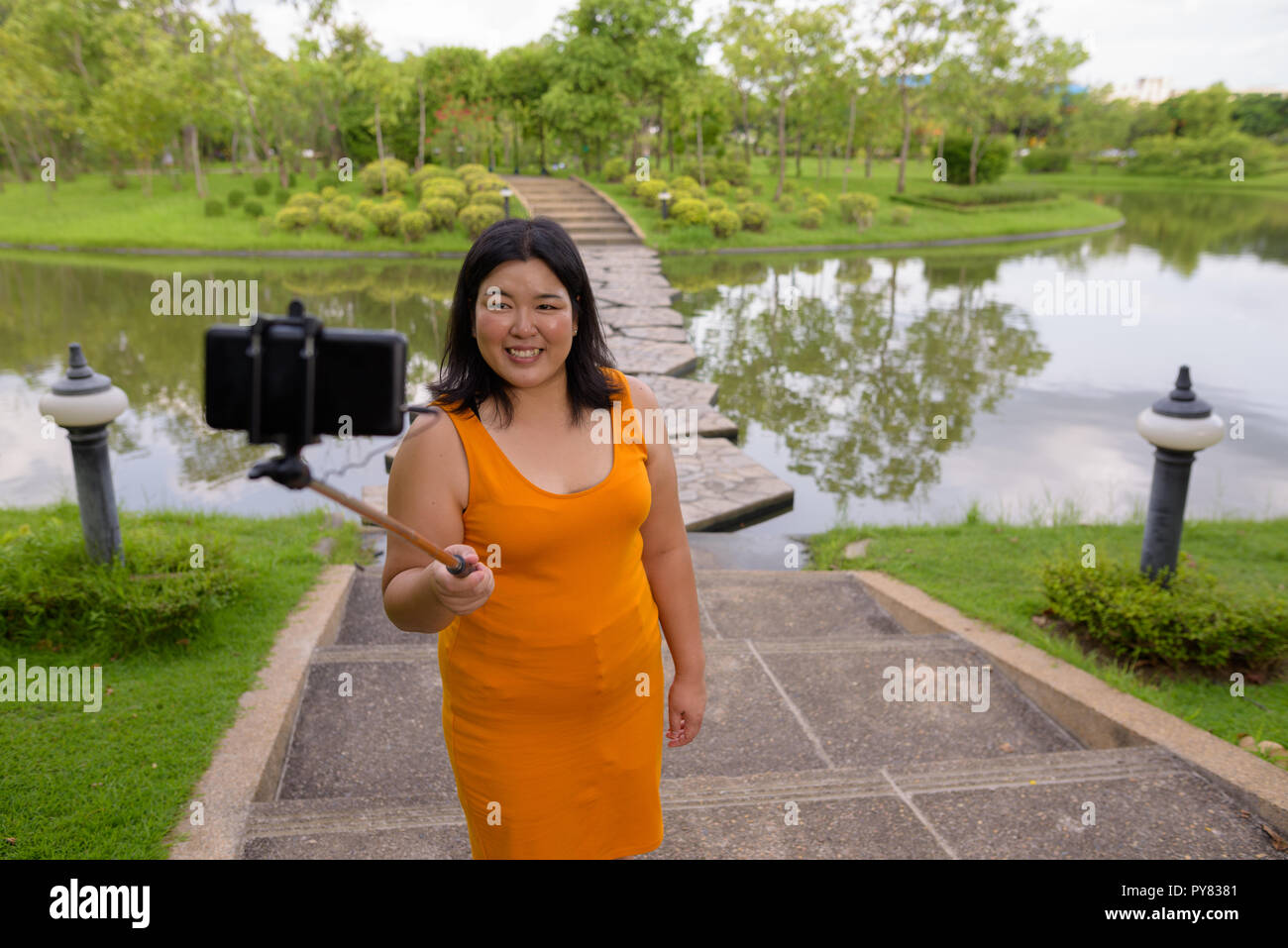 Asian woman taking selfie with mobile phone attach to selfie stick in park Stock Photo