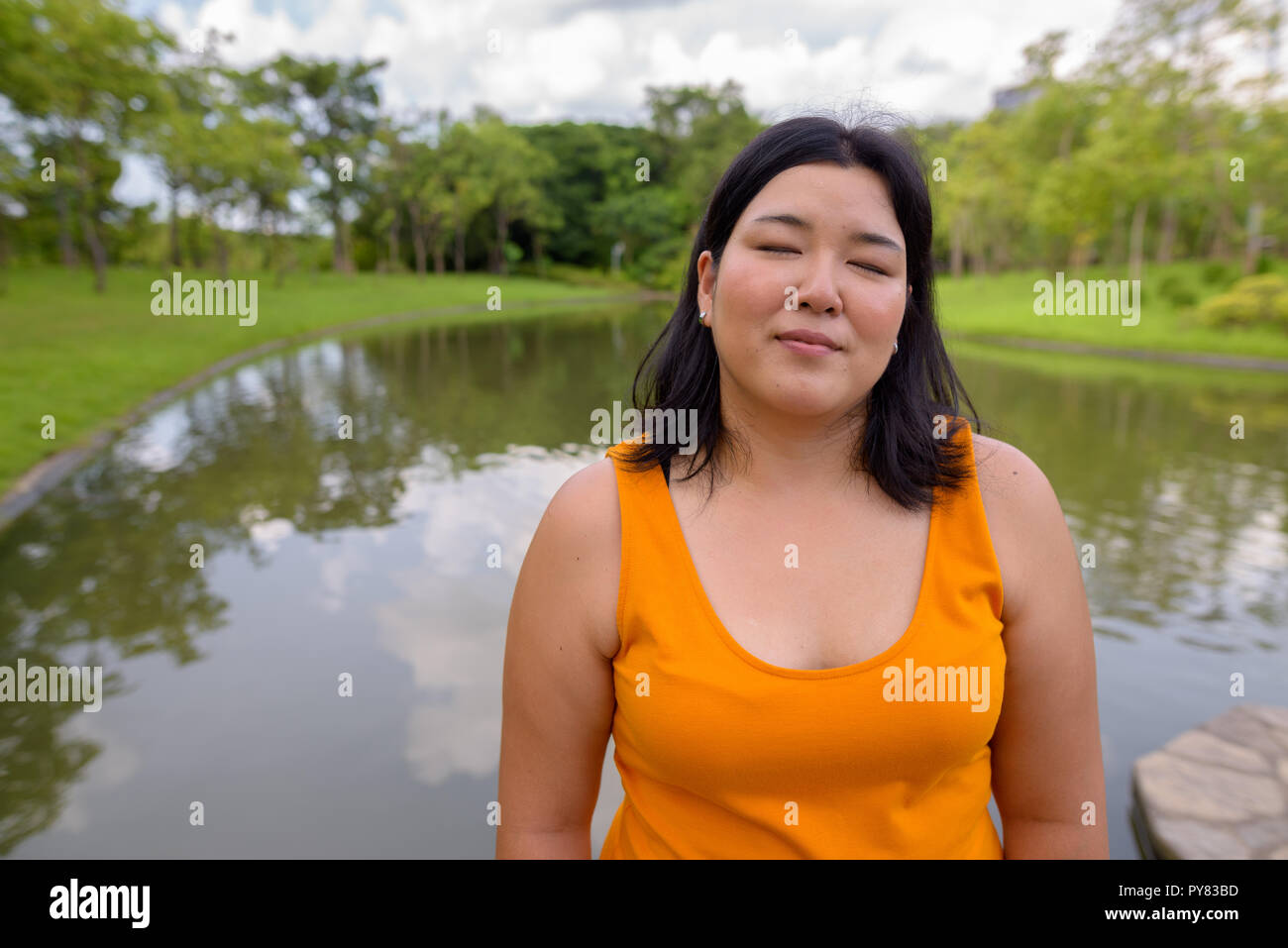 Beautiful overweight Asian woman relaxing with eyes closed in park Stock Photo