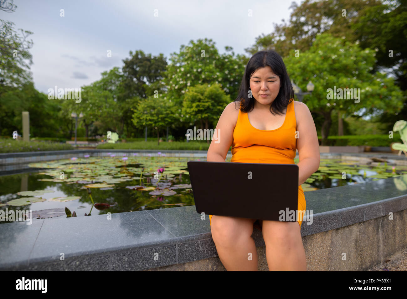 Beautiful overweight Asian woman using laptop computer in park Stock Photo