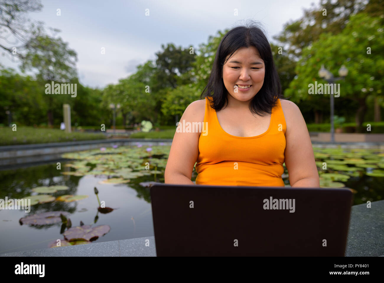 Happy overweight Asian woman using laptop computer in park Stock Photo