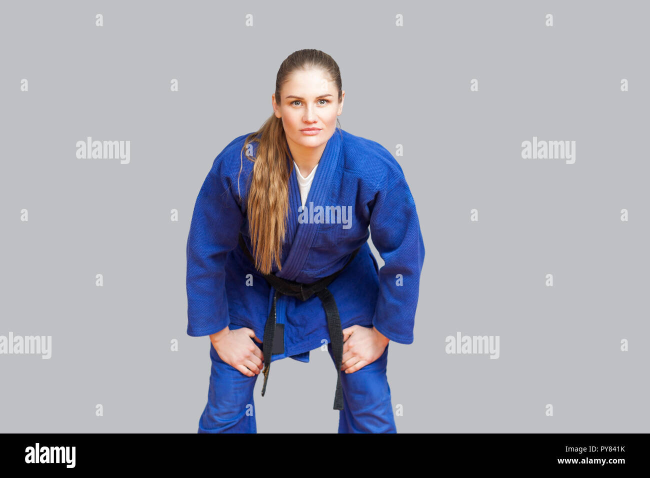 Beautiful athletic karate woman in blue kimono with black belt in fighting stance are looking at camera. Japanese martial arts concept. Indoor, studio Stock Photo