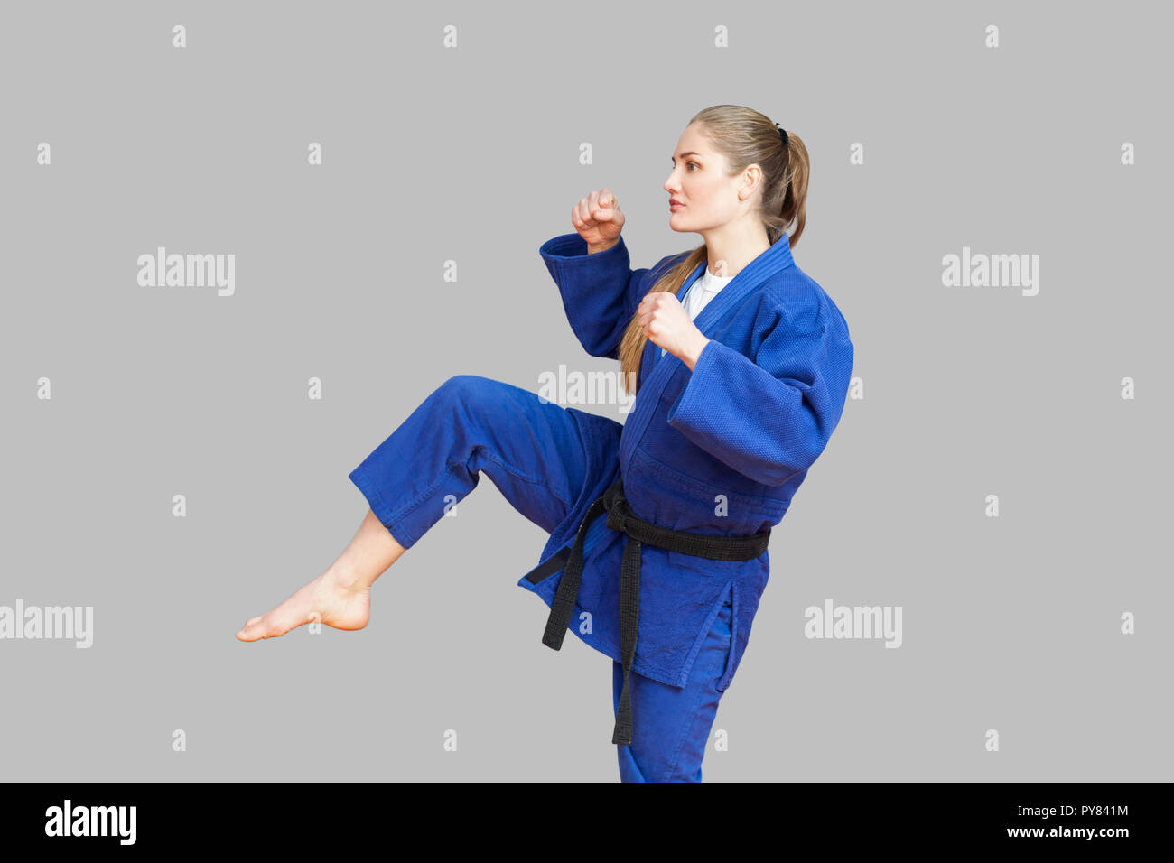 Side view of agressive athletic karate woman in blue kimono with black belt are ready to fight, punching with foot and looking away. Japanese martial  Stock Photo