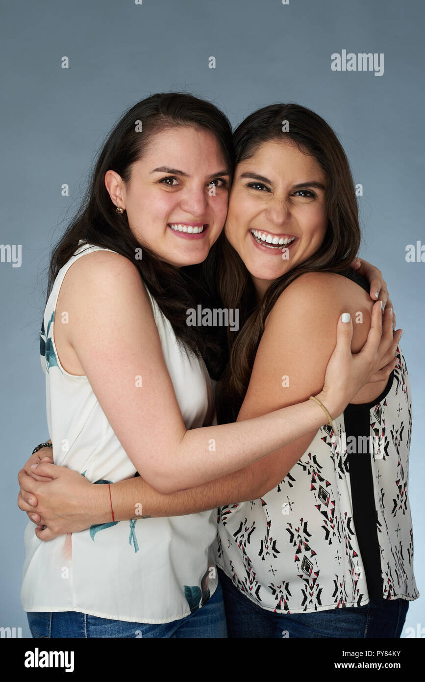 Two happy smiling latino girls hugging on gray studio background Stock Photo