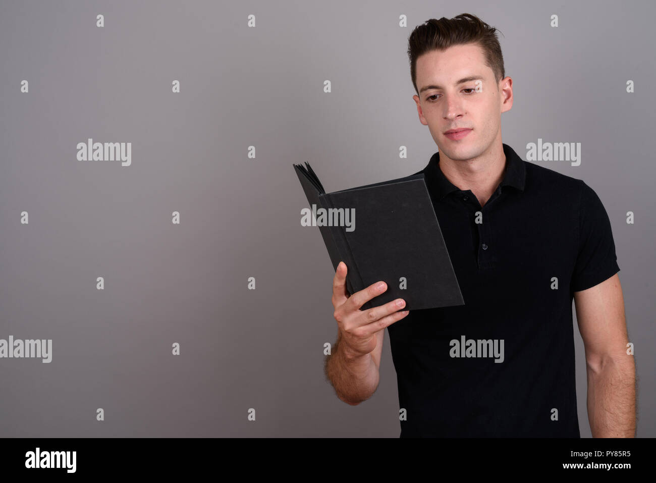 Young handsome man reading book against gray background Stock Photo