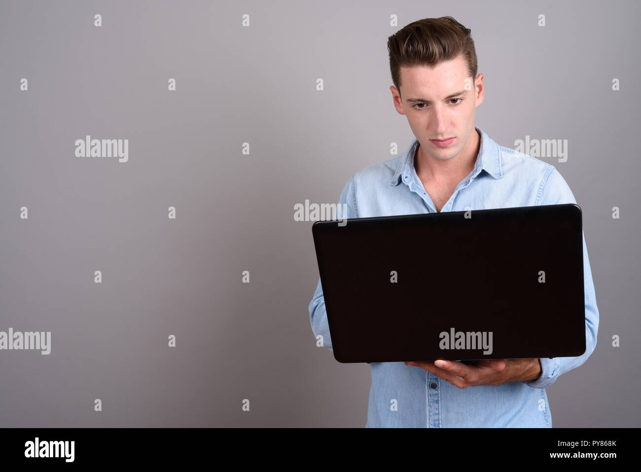 Young handsome man using laptop computer against gray background Stock Photo