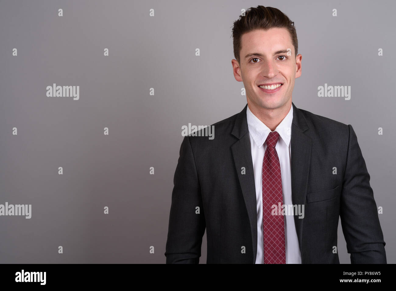 Young happy businessman wearing suit against gray background Stock Photo