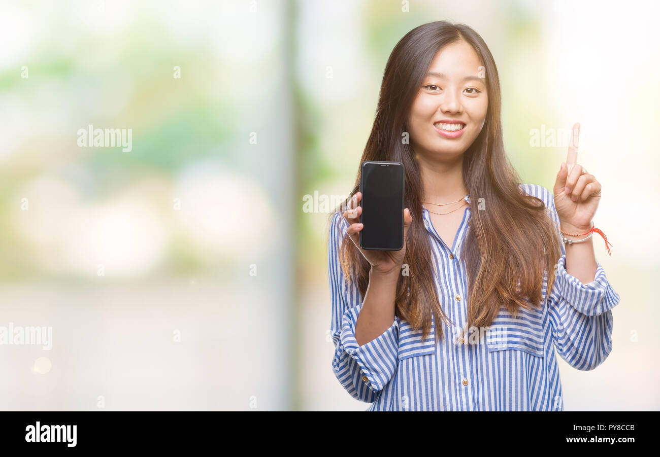 Young asian woman showing blank screen of smartphone over isolated