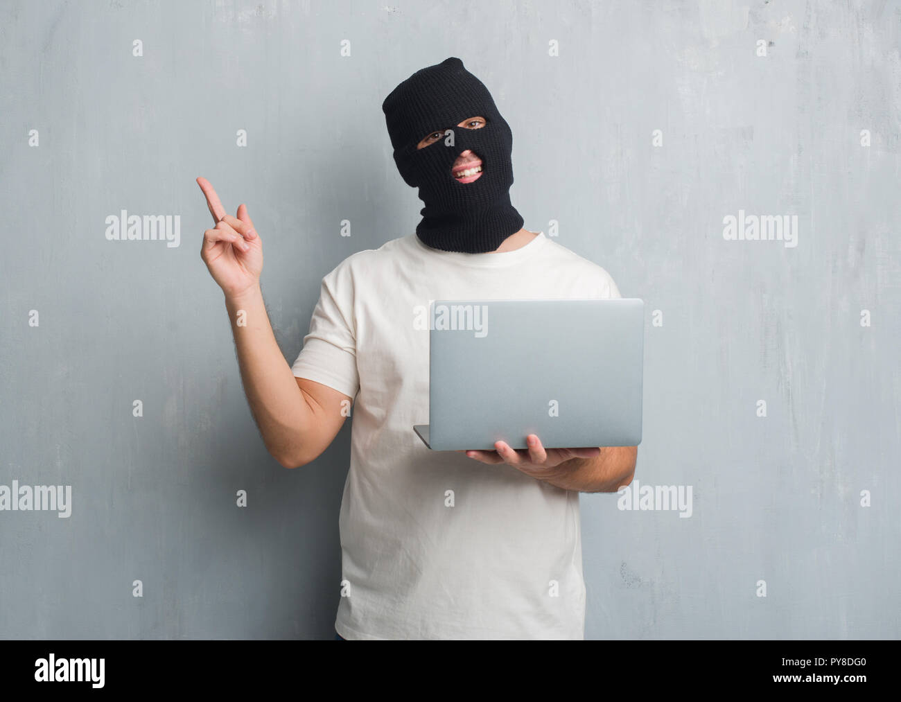 Young caucasian hacker man over grey grunge wall doing cyber attack using laptop very happy pointing with hand and finger to the side Stock Photo