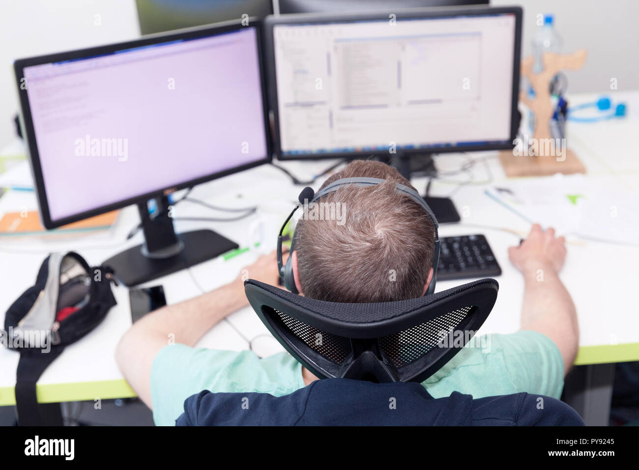 A man working on computer in an IT office, two monitors in front of him on the desk. Stock Photo