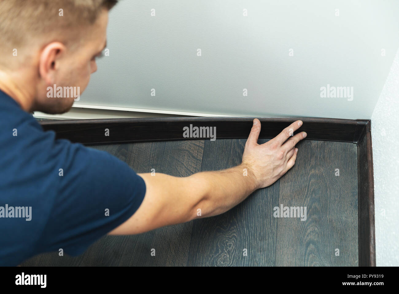 worker installing plastic baseboard on the laminate floor Stock Photo