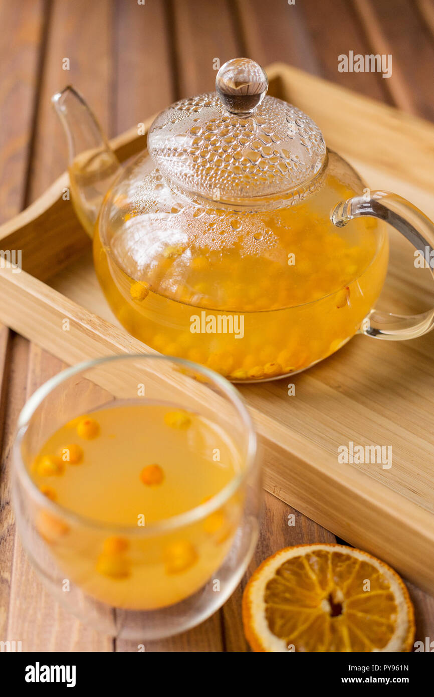 Glass teapot with sea buck thorn tea with ginger at wooden tray on wooden background Stock Photo