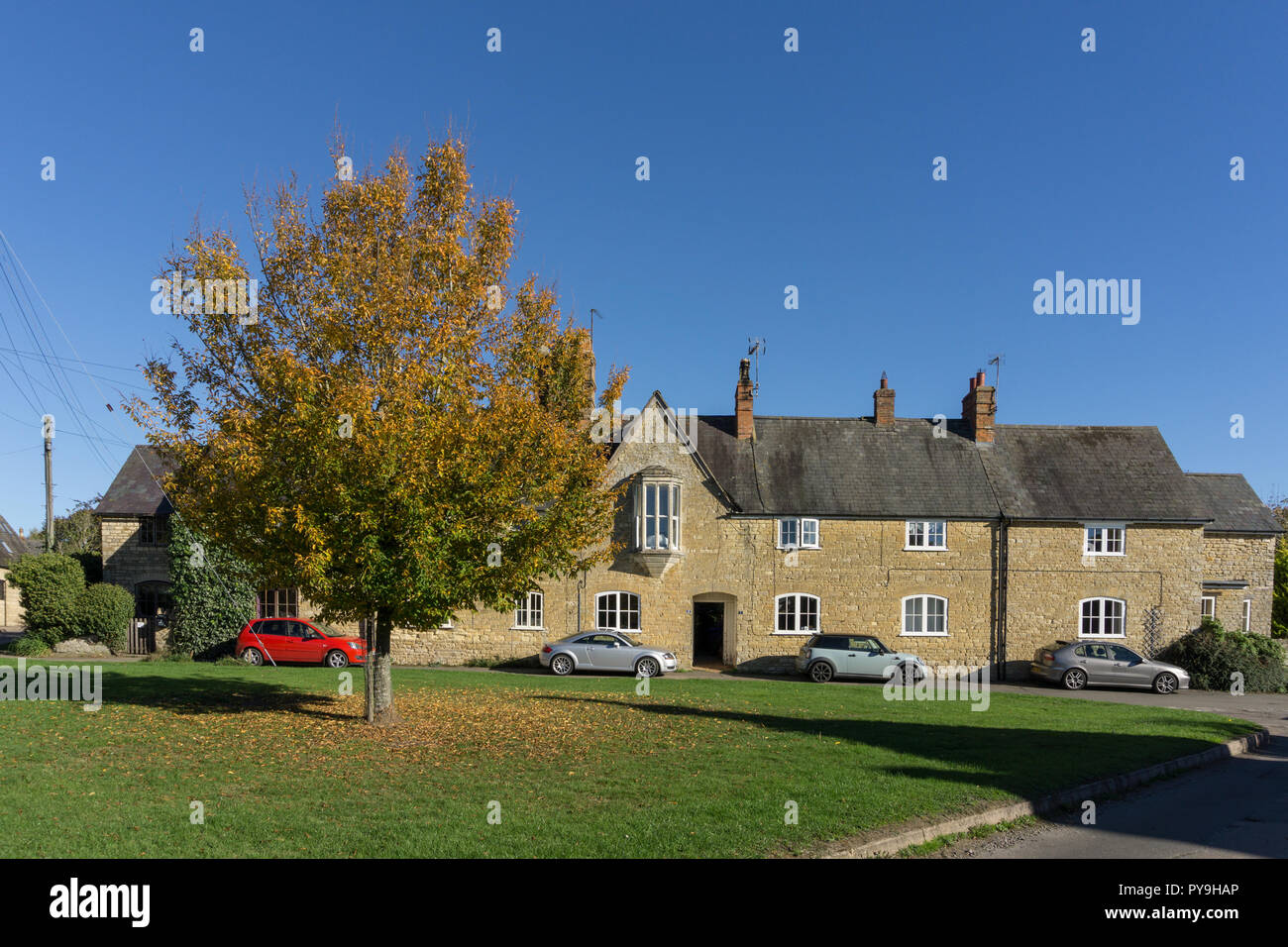 A view across the village green, with a stone built terrace of houses to the rear; Paulerspury, Northamptonshire, UK Stock Photo