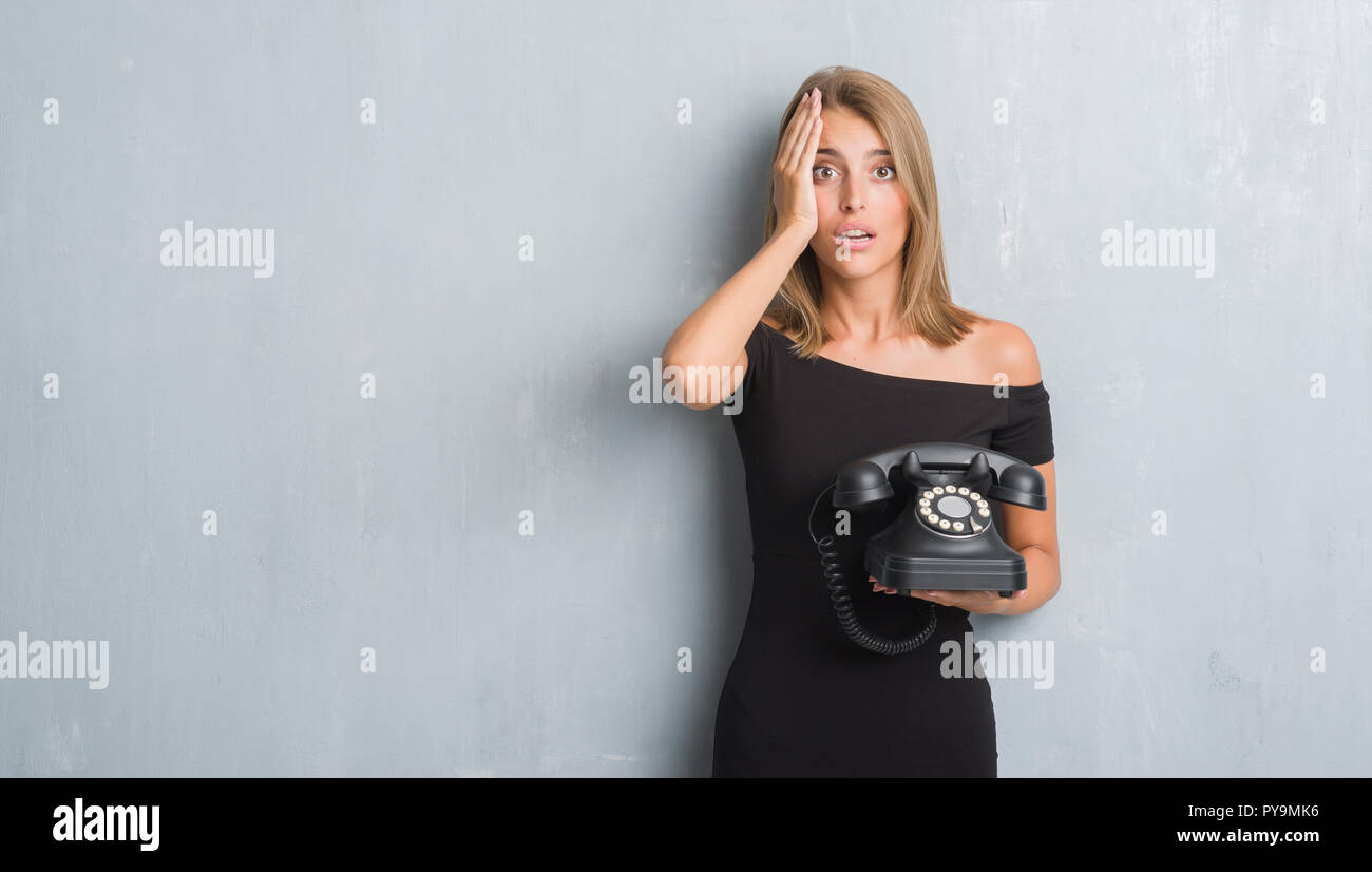 Beautiful young woman over grunge grey wall holding vintage telephone stressed with hand on head, shocked with shame and surprise face, angry and frus Stock Photo