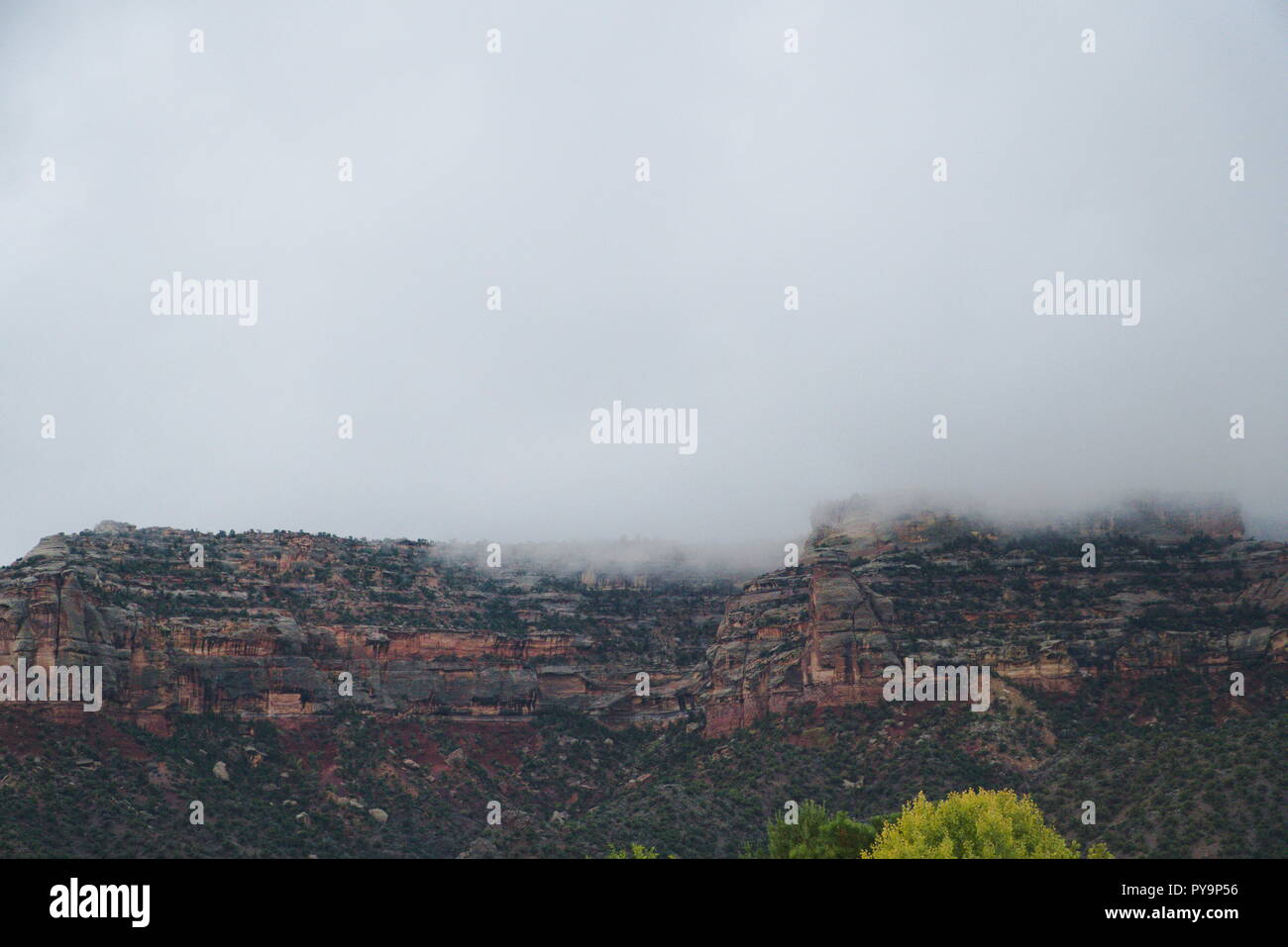 The Colorado National Monument shrouded by a layer of heavy fog. The clouds above are grey and gloomy. There is an overall downcast vibe. Stock Photo