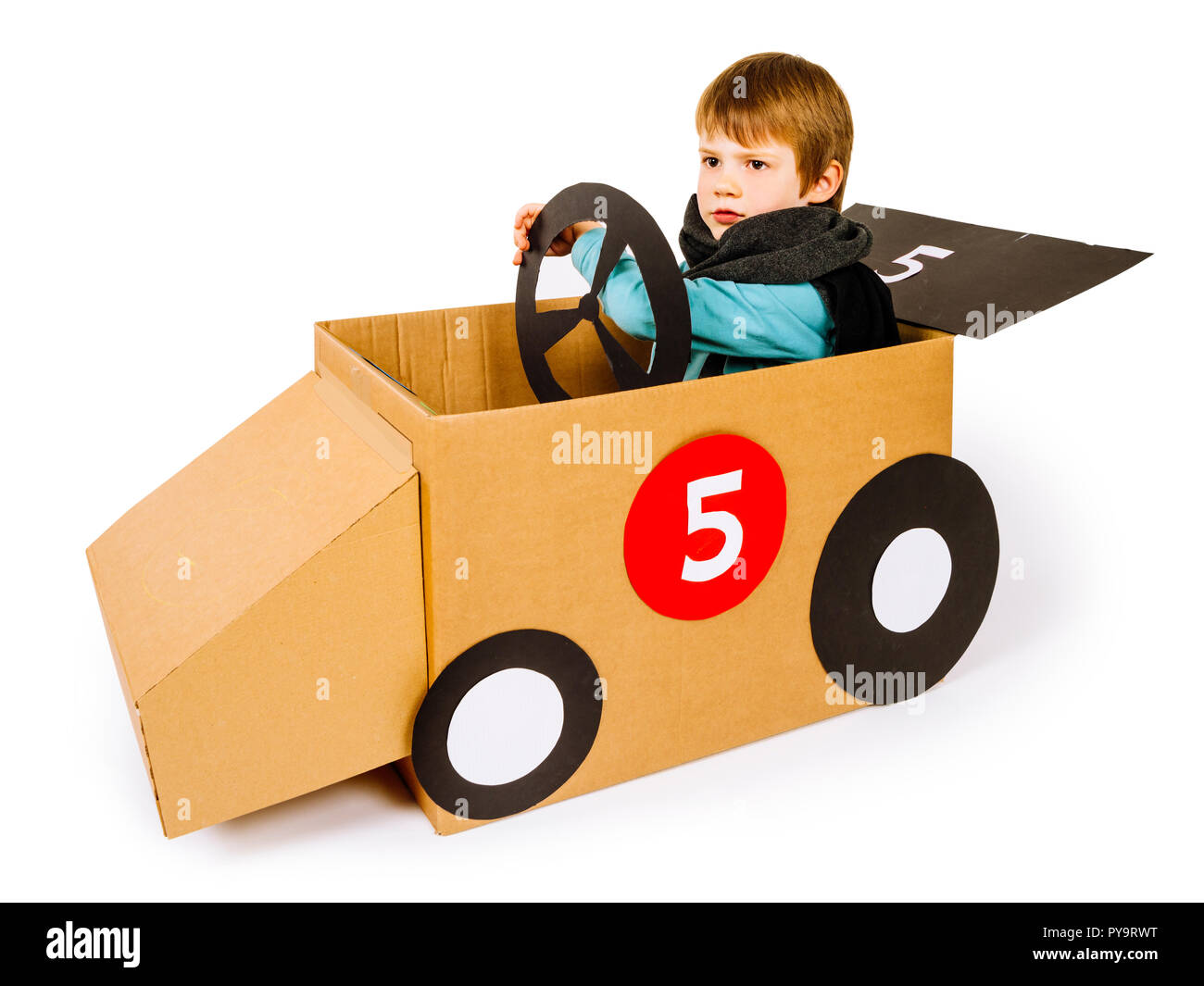 Photo of a young boy driving his homemade cardboard car over white background. Stock Photo