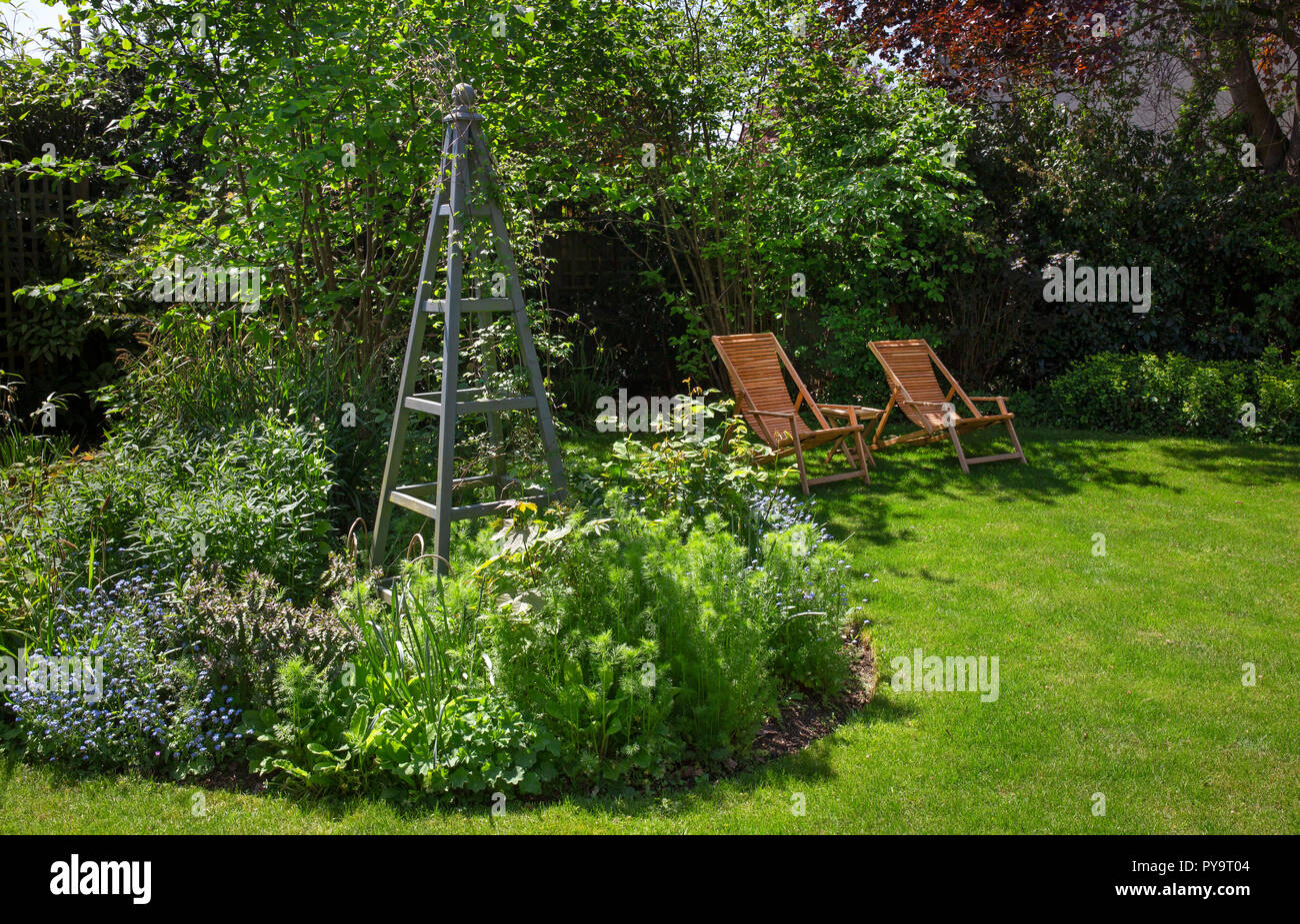 Summer boarder with wooden obelisk plant support feature and wooden garden chairs in English Garden,England,Europe Stock Photo