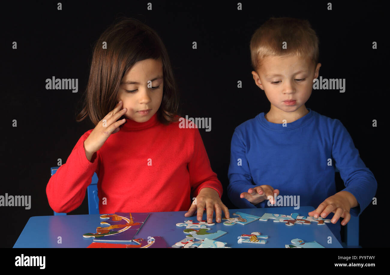 Brother and sister playing with a puzzle on a blue table with a black background Stock Photo