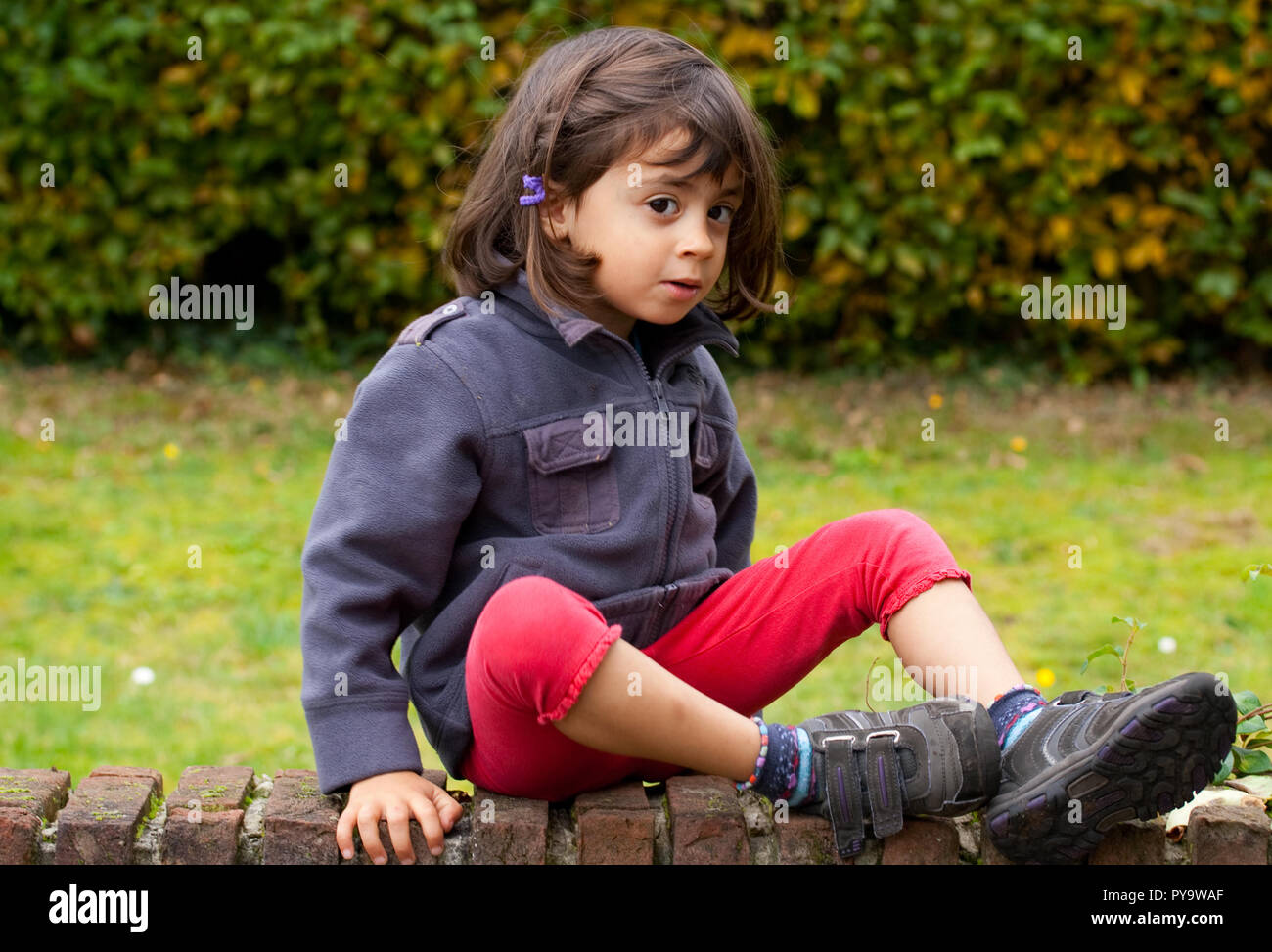 Little girl sitting on a brick wall Stock Photo