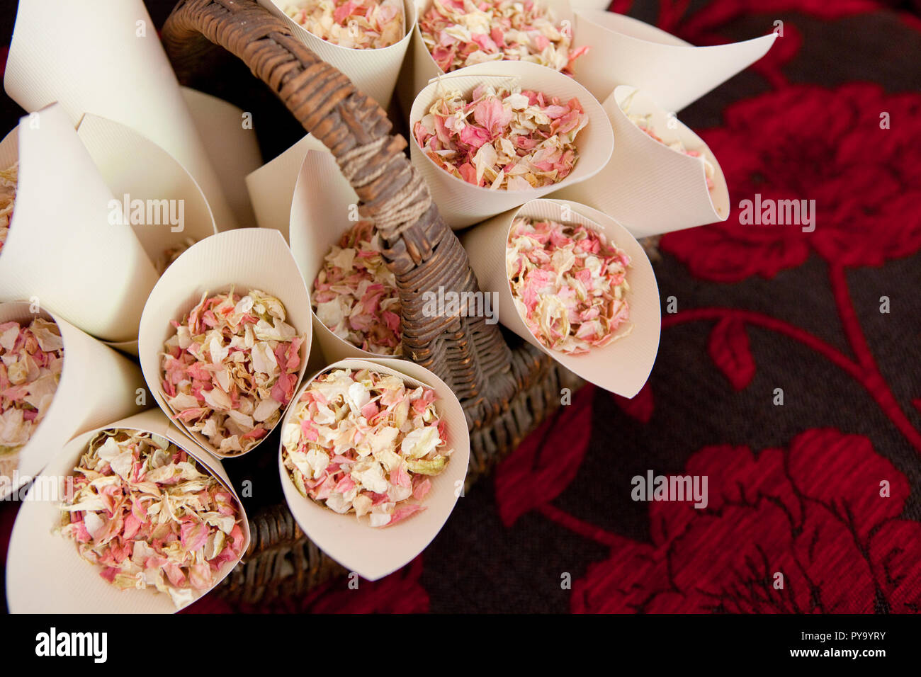 A brown wicker basket of natural dried petal confetti cones sat on a dark coloured sofa Stock Photo