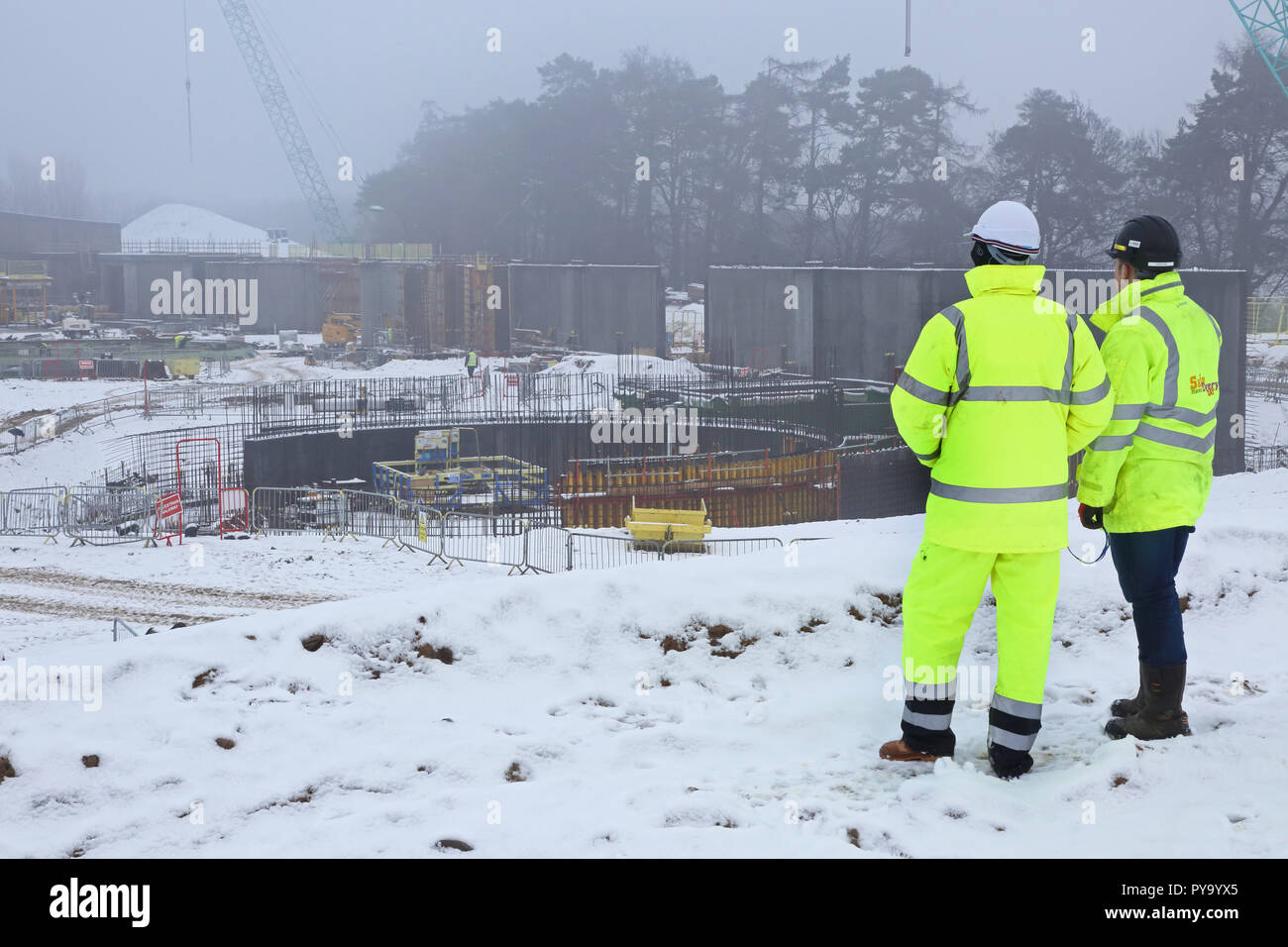 Two construction workers view a large building site in Scotland with work halted by heavy snowfall Stock Photo
