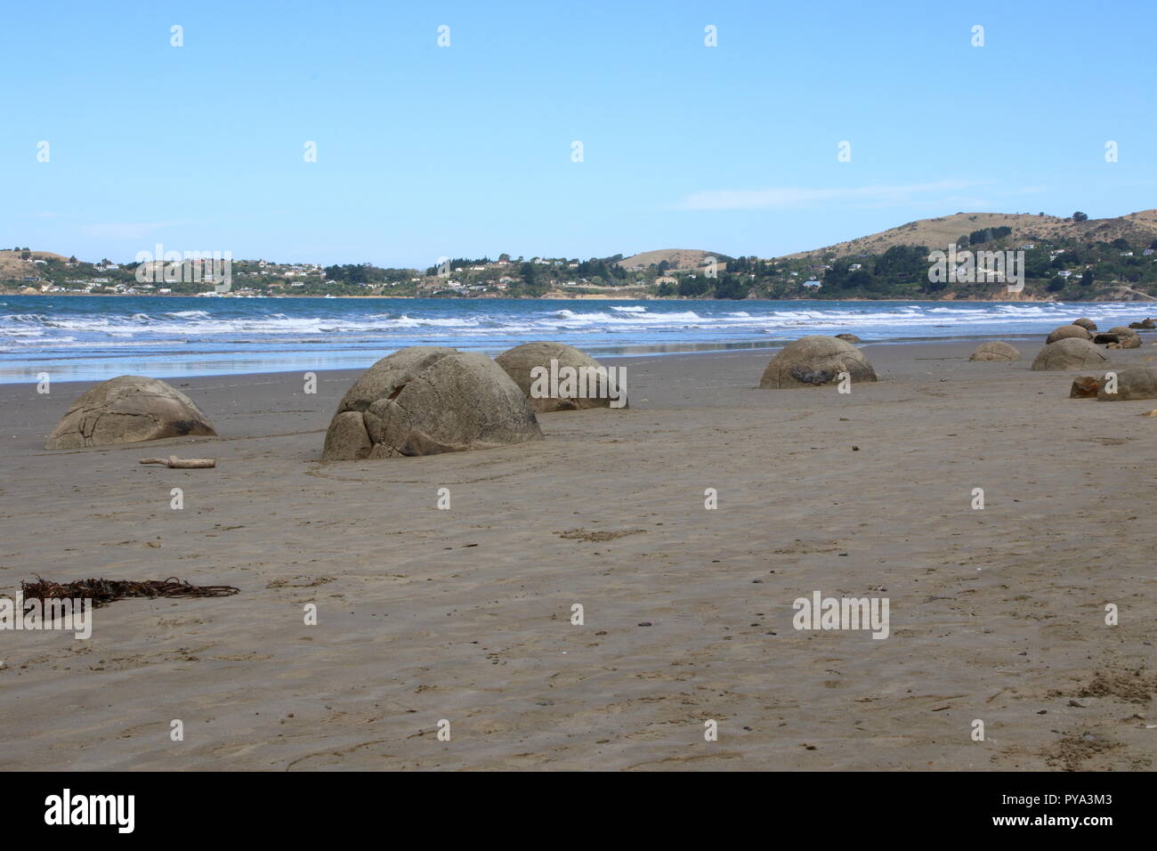 Moeraki beach looking across the bay with boulders in the foreground on the sandy tourist beach. Stock Photo