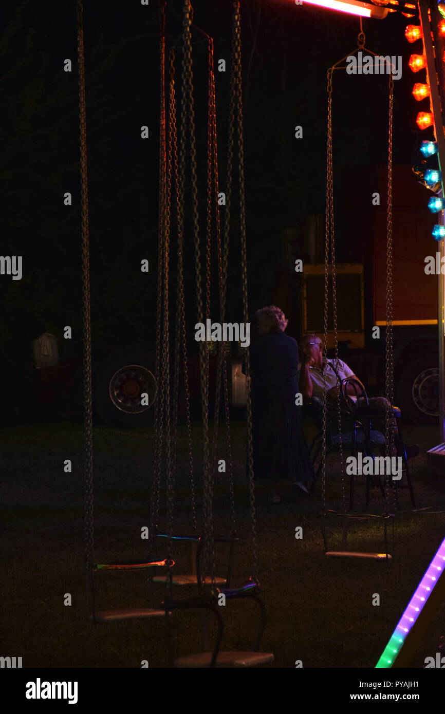 Old couple looking their grandchildren in an amusement park at night Stock Photo