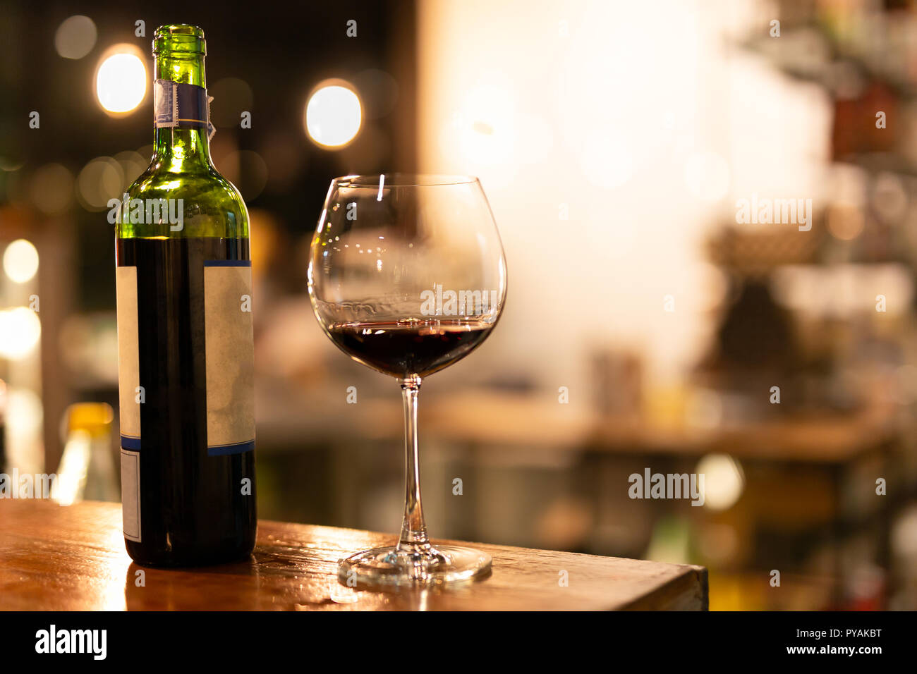 Shot in low light and high iso bottle and glass of red wine on wooden top. Stock Photo