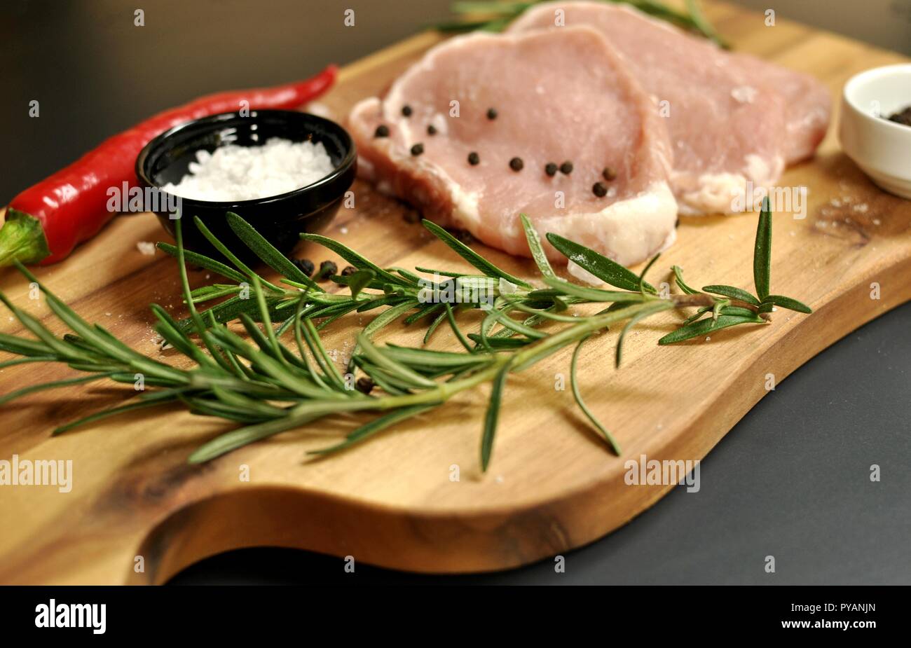 Raw fresh uncooked sliced pork fillet  dish with rosemary, pepper, salt, red chili pepper on wooden board and black background. Top side view Stock Photo